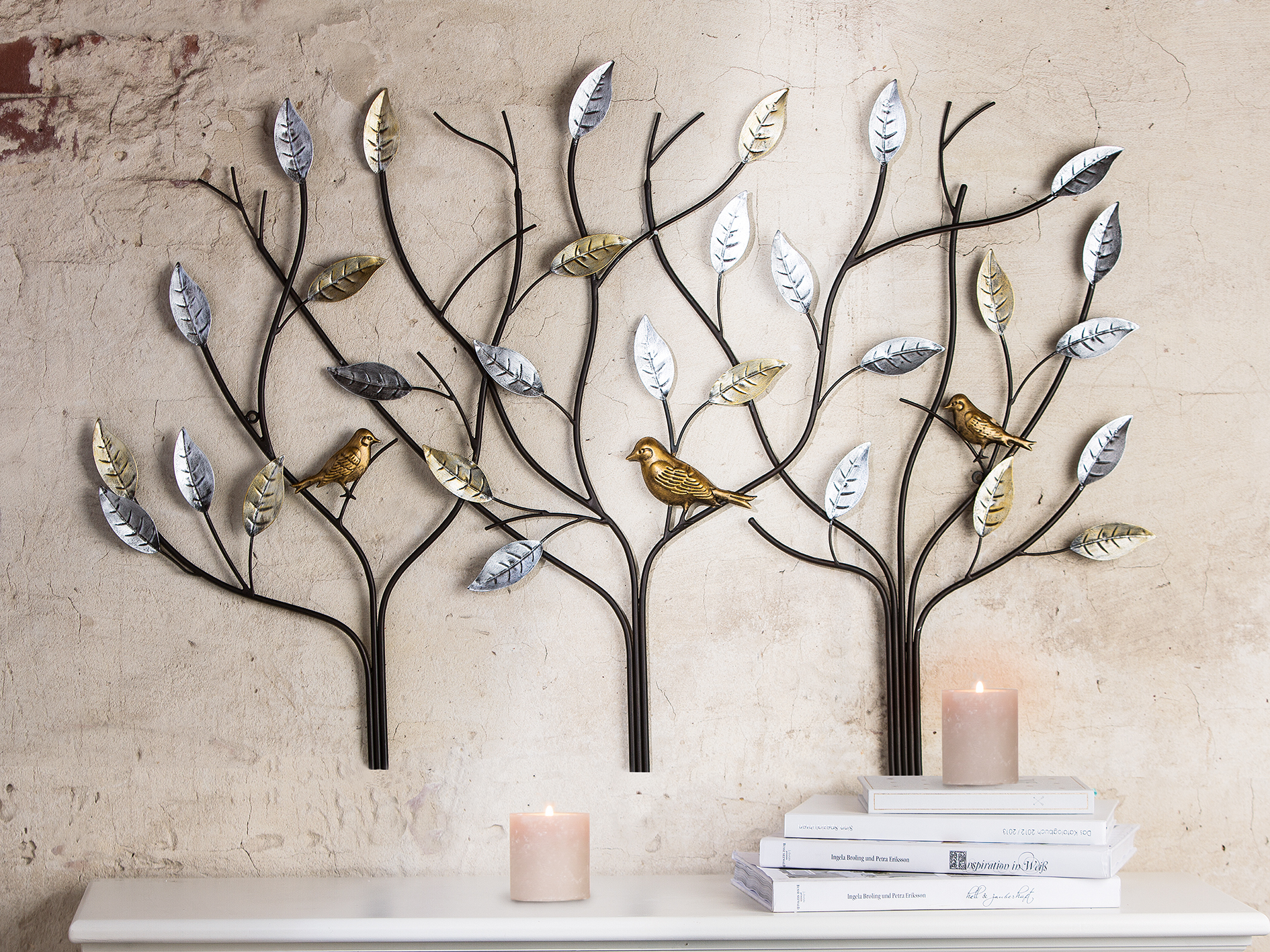 Een wanddecoratie met metalen takken en bladeren in verschillende kleuren, inclusief gouden en zilveren vogels.