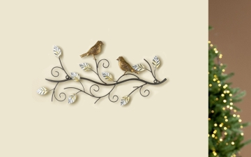 Twee gouden vogels zitten op een metalen tak met glanzende bladeren tegen een lichte achtergrond, sfeervol verlicht.