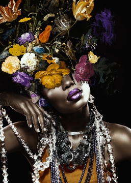 Een vrouw met een explosie van kleurrijke bloemen als hoofdtooi, sieraden van kristal en een glanzende paarse lipkleur.
