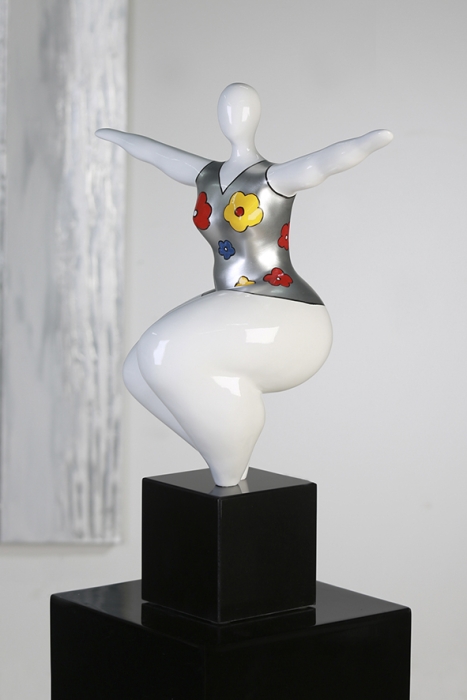 Gestileerde sculptuur van een vrouw met een glanzend zilveren top versierd met bloemen in rood, geel en blauw, op een zwarte sokkel.