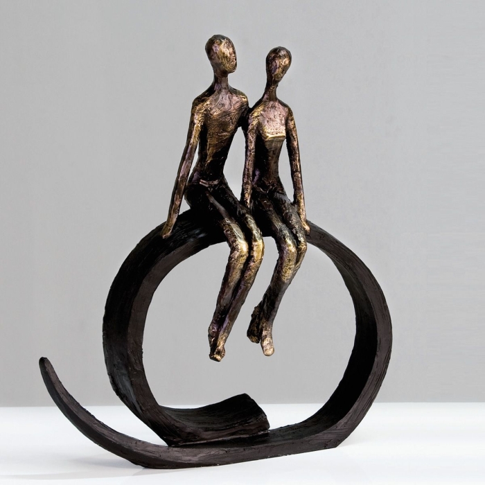 Twee abstracte figuren in brons en zwart, zittend op een golvende basis, met gedetailleerde textuur en een moderne uitstraling. Twee abstracte figuren in brons en zwart, zittend op een golvende basis, met gedetailleerde textuur en een moderne uitstraling.