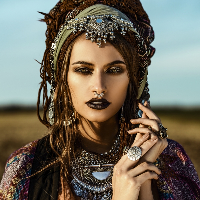 Een vrouw met dreadlocks en opvallende sieraden poseert in een natuurlijke omgeving, met een dramatische make-up en een kleurrijk kledingstuk. Een vrouw met dreadlocks en opvallende sieraden poseert in een natuurlijke omgeving, met een dramatische make-up en een kleurrijk kledingstuk.
