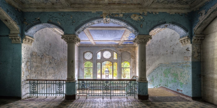 Verweerd trappenhuis met blauwe muren, ornamenten, en een houten leuning, verlicht door natuurlijk licht via grote ramen. Verweerd trappenhuis met blauwe muren, ornamenten, en een houten leuning, verlicht door natuurlijk licht via grote ramen.